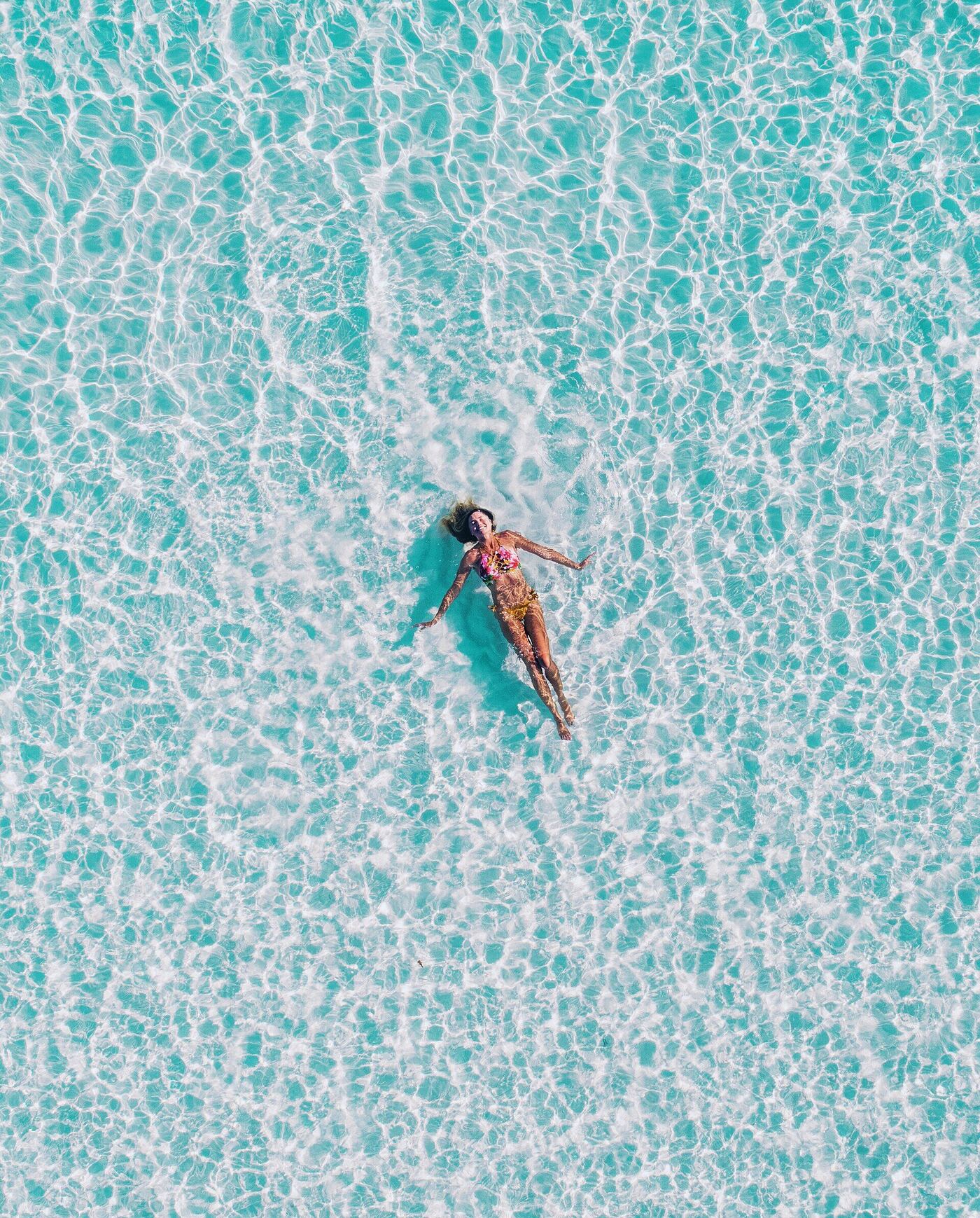 A swimmer floating in a turquoise Maldivian lagoon, seen from above